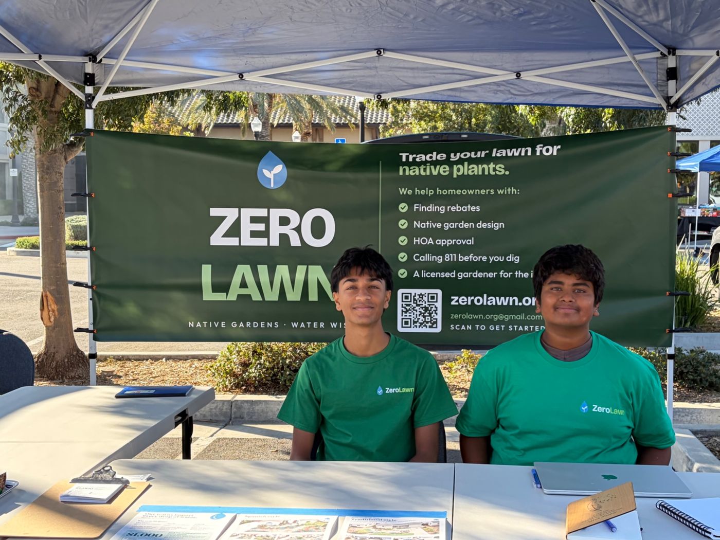 Two ZeroLawn students seated at the booth table in front of the ZeroLawn banner